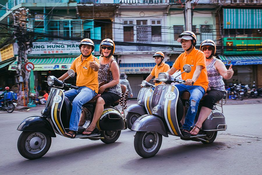 Taste of Saigon by scooter! Dive into Ho Chi Minh City’s street food scene like a local People on scooters enjoying a street food tour in Saigon (Ho Chi Minh City), with food stalls visible