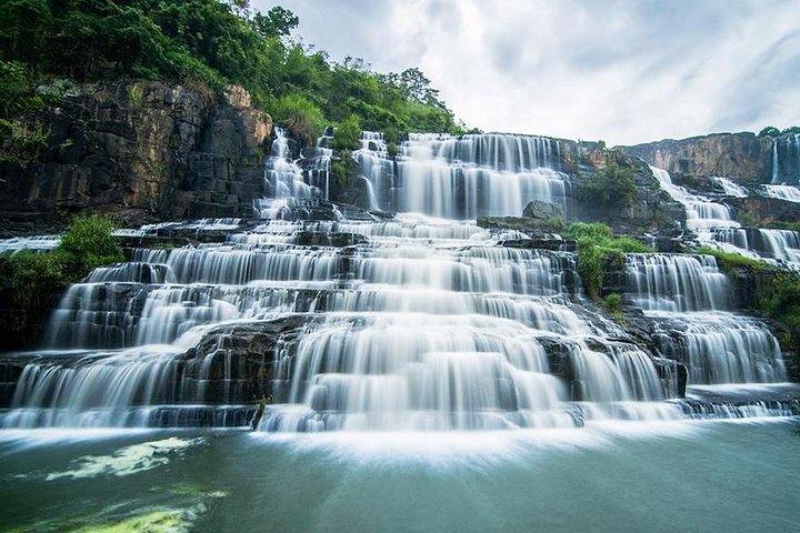 Uncover Dalat’s hidden magic! Explore misty waterfalls tucked away in lush pine forests and secret caves. A traveler discovering the misty, hidden cascades of Elephant Waterfall surrounded by lush green jungle foliage.