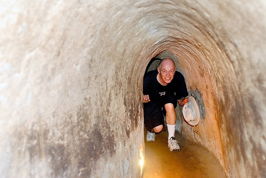 Crawling through history: Experience the incredible ingenuity and resilience inside the legendary Cu Chi Tunnels, Vietnam. People navigating a narrow, dark section of the Cu Chi Tunnels in Vietnam, showing the underground network.