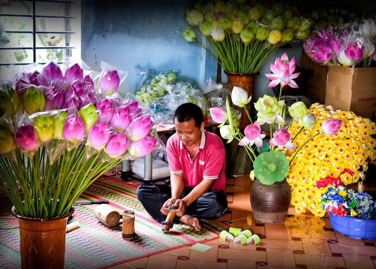 Learning the beautiful tradition of paper flower craftsmanship in Thanh Tien village. A tourist making a paper flower with an artisan in a Hue craft village.