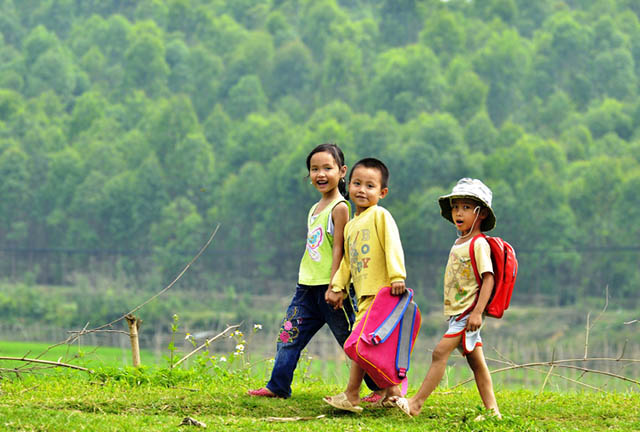 A glimpse into authentic local life: children happily riding their bikes to school in Hue. Local children in school uniforms riding bicycles on a country road in rural Hue, Vietnam.