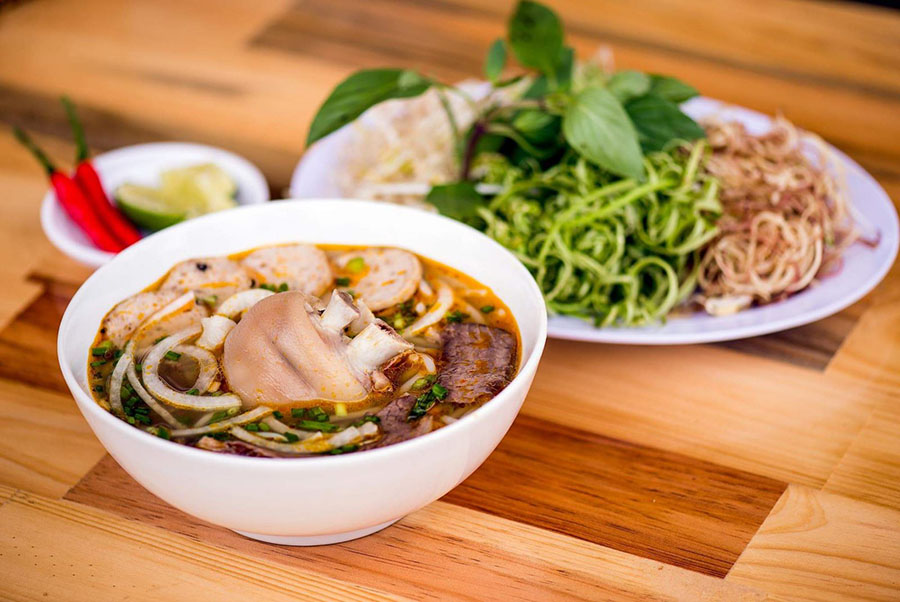 Taste the legendary Hue beef noodle soup (Bún bò Huế), a local culinary masterpiece. A vibrant bowl of Hue beef noodle soup with beef, herbs, and thick rice noodles.